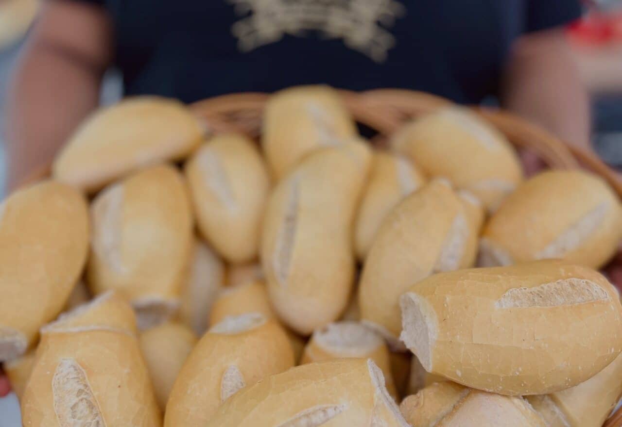 Funcionário com o brasão bordado na camiseta segurando uma cesta cheia de pães franceses