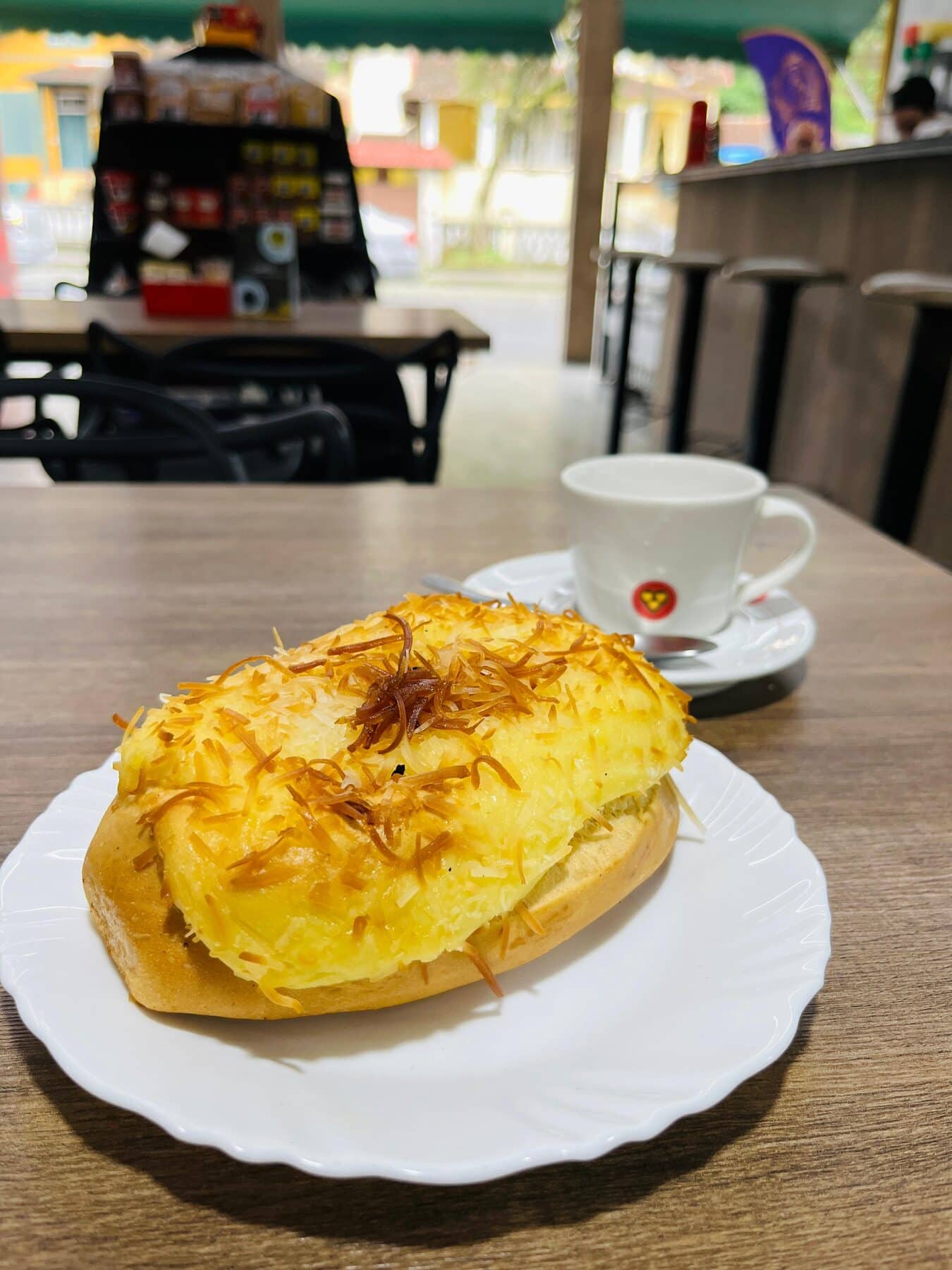 Pão gratinado com queijo e batata palha em prato branco, com uma xícara de café ao fundo